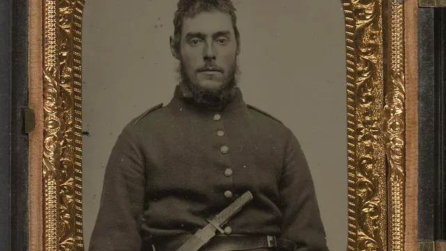 Ambrótipo colorido à mão de um soldado da União, entre 1861 e 1865, sentado de uniforme com uma faca bowie de lâmina larga presa ao cinto, a mão direita apoiada sobre o cabo.