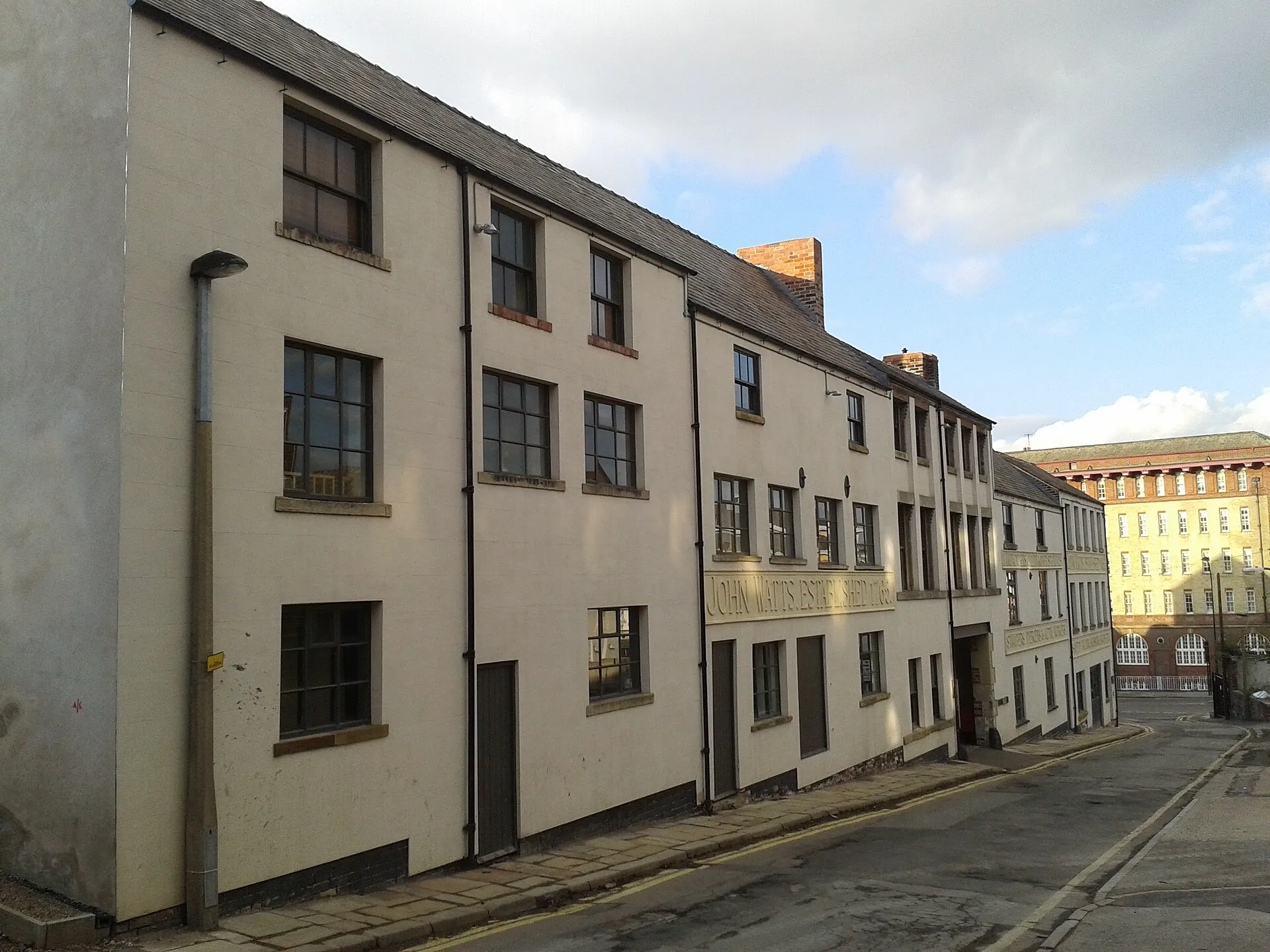 Prédio industrial de tijolos de várias janelas, antiga fábrica de cutelaria John Watts, numa rua de Sheffield