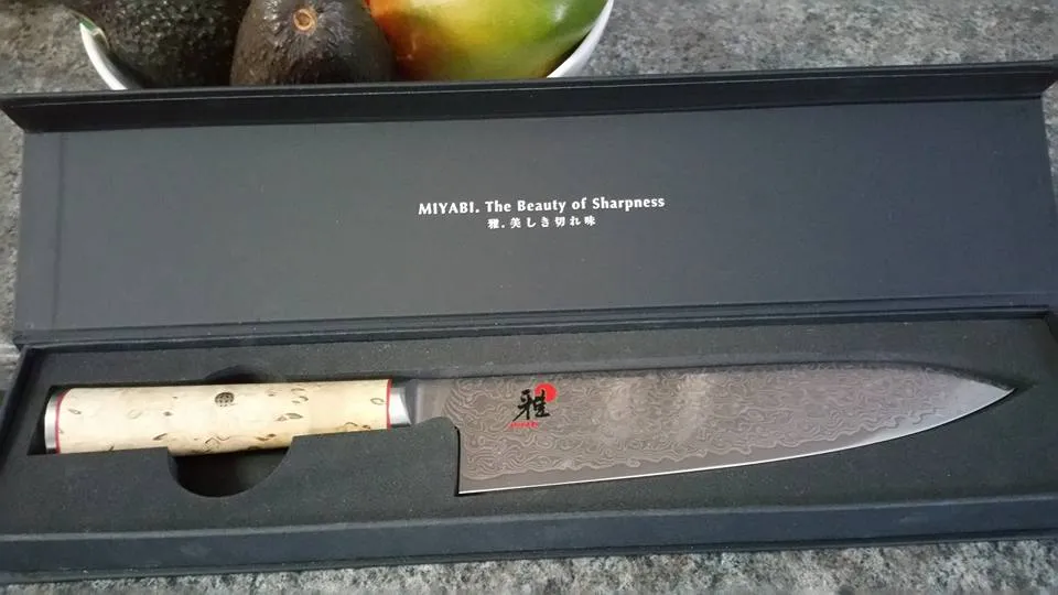 Faca japonesa gyuto Miyabi 5000MCD dentro da caixa, com lâmina de padrão damasco visível e cabo de madeira de bétula com anel vermelho.