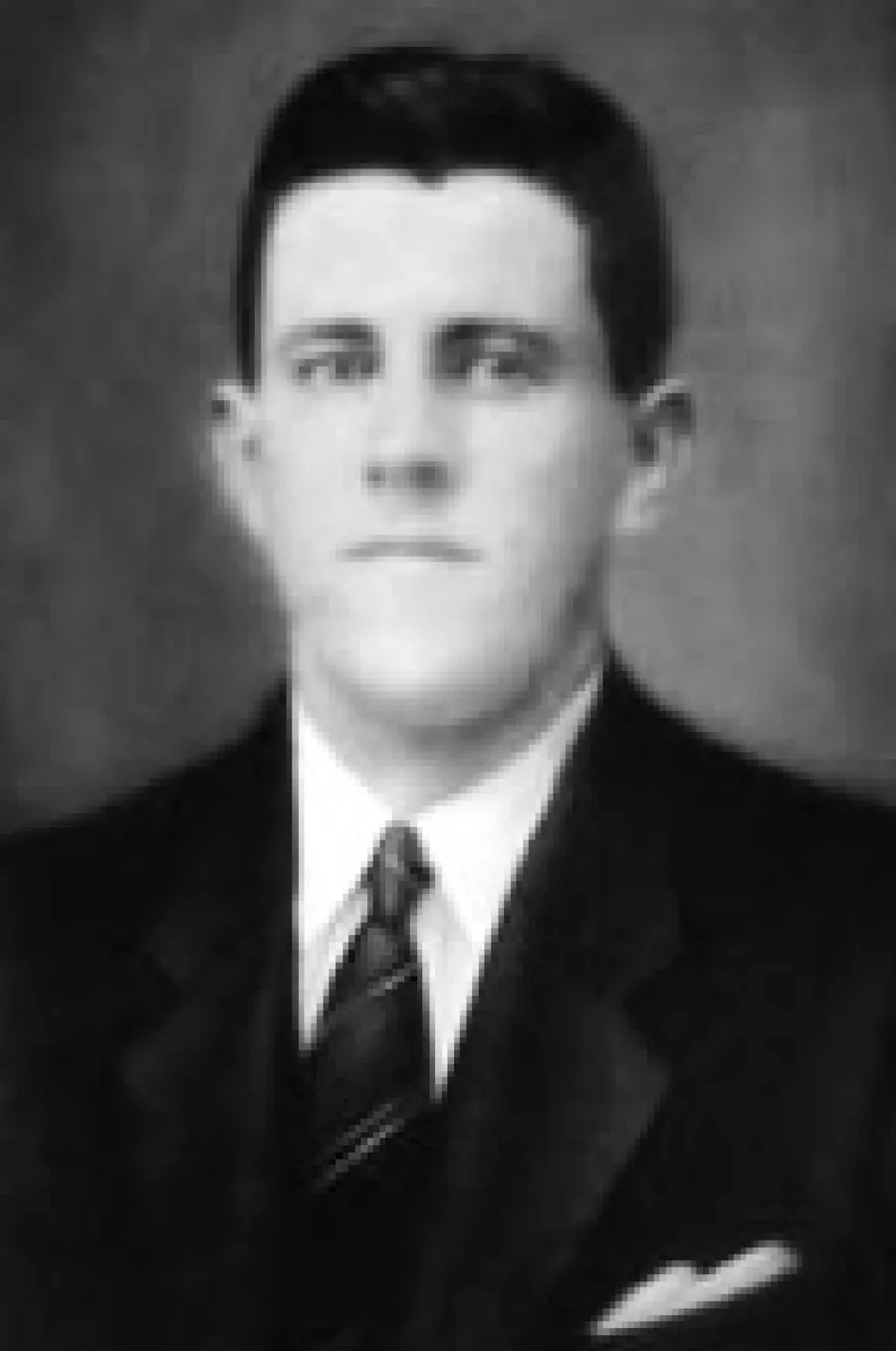 Retrato de estúdio em preto e branco de um homem jovem, de terno escuro e gravata, cabelo curto penteado para trás, olhando sério para a câmera